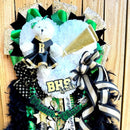 Decorative homecoming mum with ribbons, feathers, and a teddy bear on a wooden background